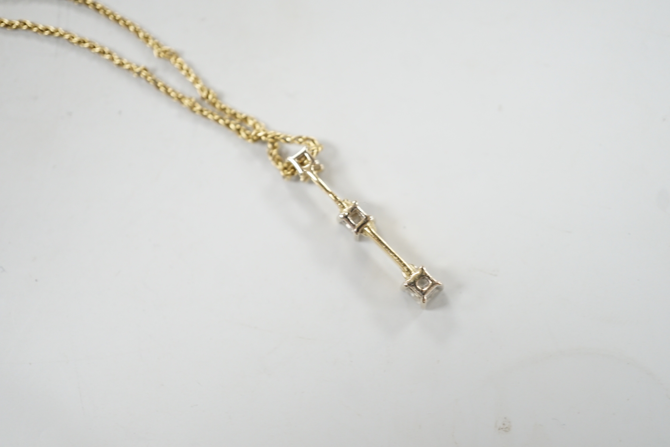 A modern yellow metal and graduated three stone princess cut diamond set line pendant, 25mm, on a 750 chain, 38cm, gross weight 4.5 grams.